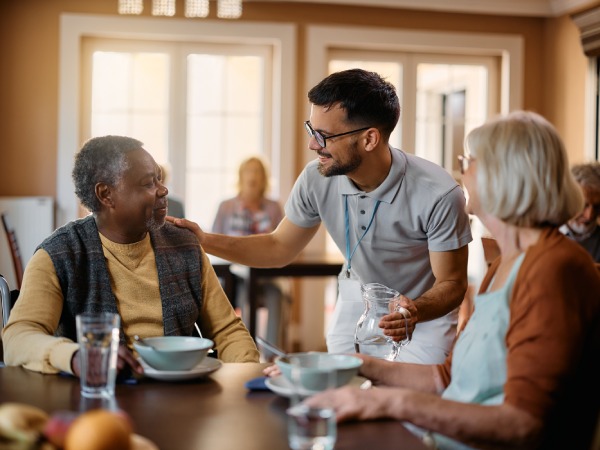 Young healthcare worker talking to seniors during lunch at nursing home.