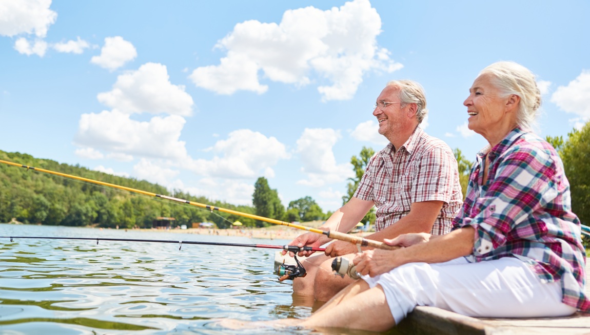 Happy senior couple relaxes while fishing together by the lake in summer