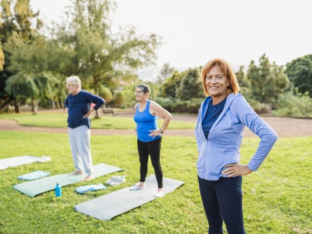 Multiracial senior people doing workout exercises outdoor with city park in background - Healthy lifestyle and joyful elderly lifestyle concept - Focus on latin woman face