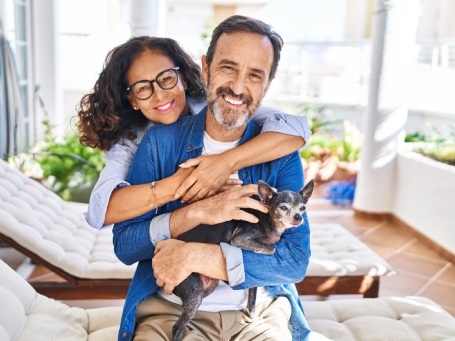 Middle age hispanic couple hugging each other sitting on hammock with dog at terrace